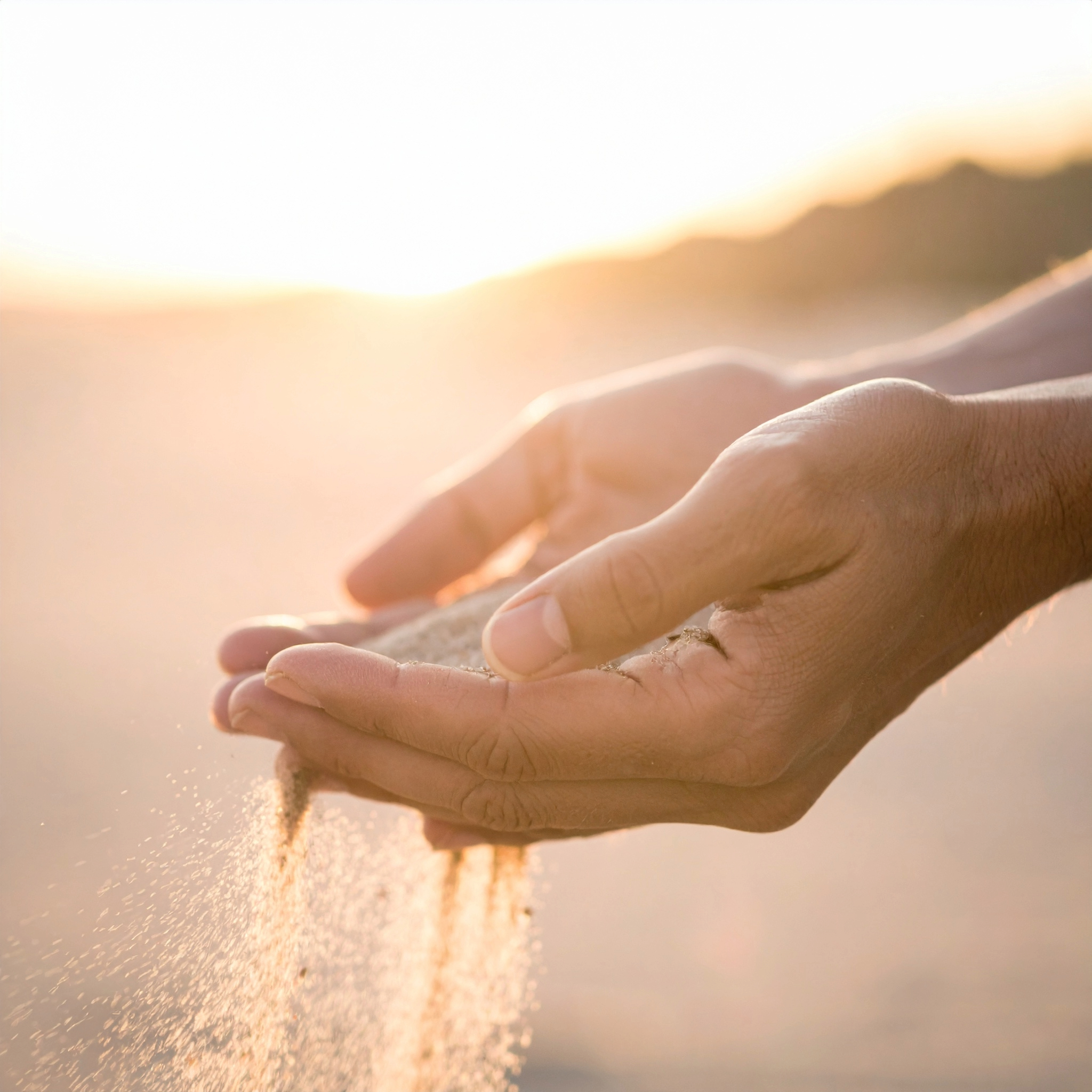 Hands pouring sand at sunset